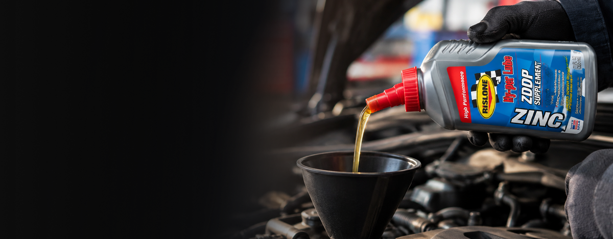 A silver and blue bottle of red line zddp supplement oil with a red cap, being poured into a black funnel.