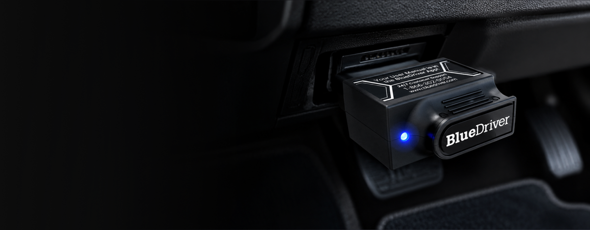 Black bluedriver device with a glowing blue light, plugged into a car’s obd2 port.