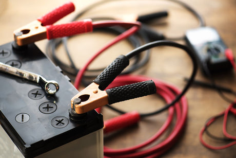 Black car battery with red and black jumper cables attached to terminals for charging with a 12v charger