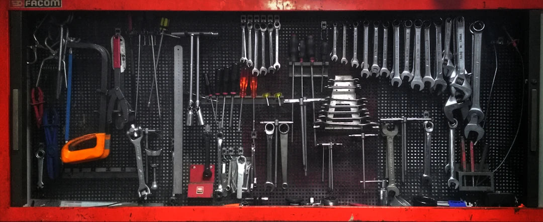 Organized collection of metallic wrenches and tools neatly arranged on a red pegboard for garage car repairs