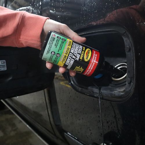 Black bottle of rislone def clean diesel dpf exhaust and emissions system cleaner with green and yellow label poured into car fuel tank