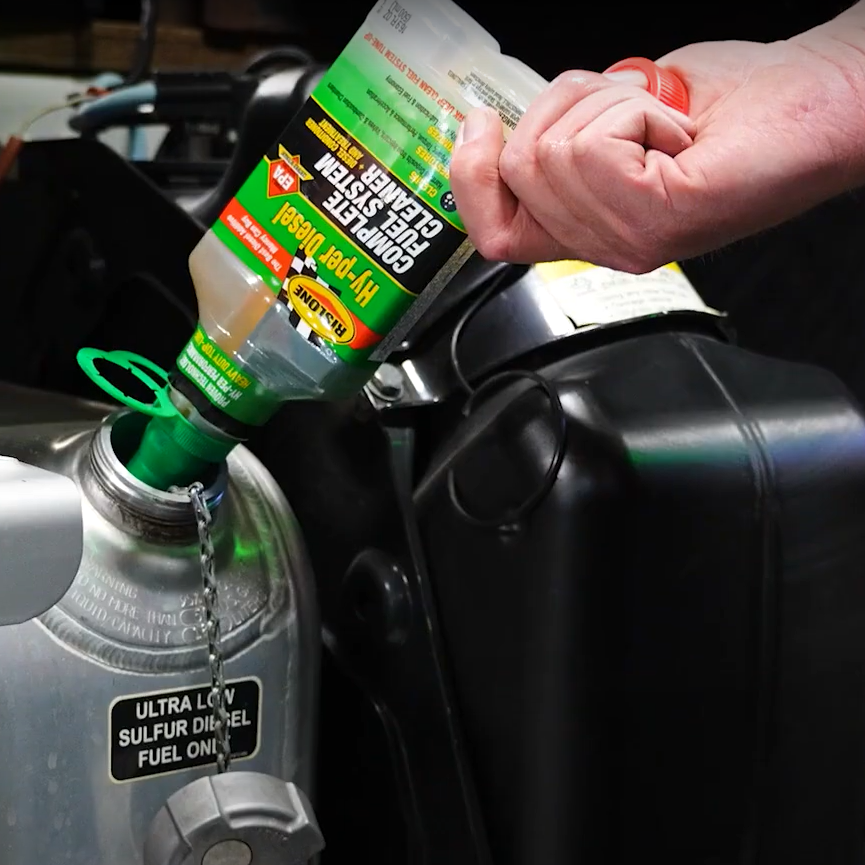 Person pouring a green bottle of Rislone Hy per Complete Fuel System for Diesel  into a fuel system component.