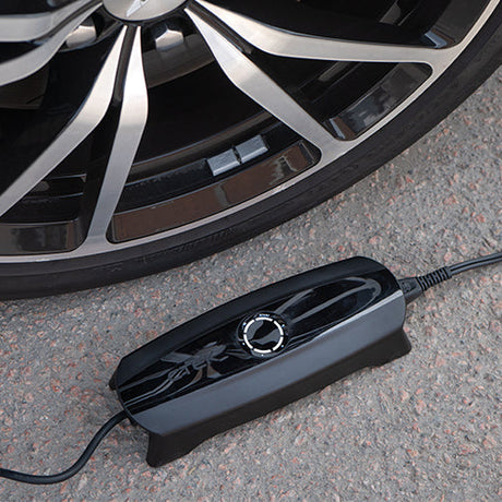 Black glossy tire inflator with circular dial and embossed design resting on asphalt beside a car wheel