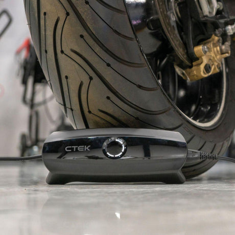 Black ctek cs one 12v smart battery charger with app control featuring a circular dial and sleek glossy finish